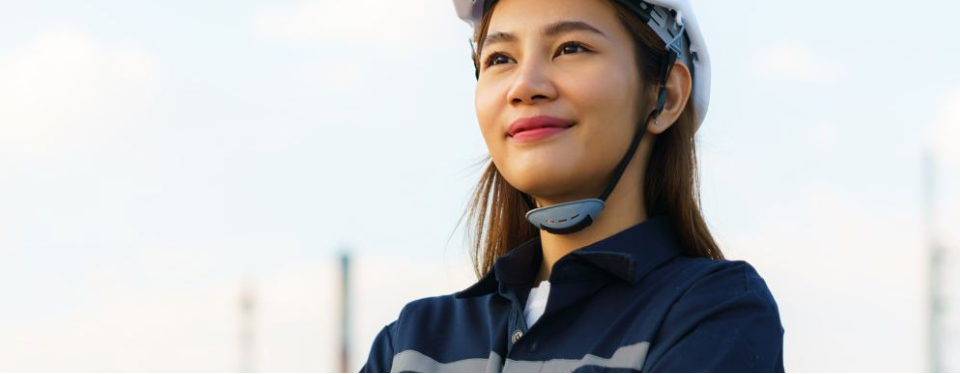 A woman in a hard hat with an industrial landscape in the background