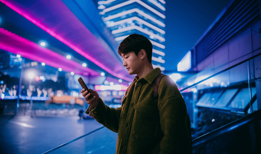 Man using a smartphone in a neon-lit city at night.