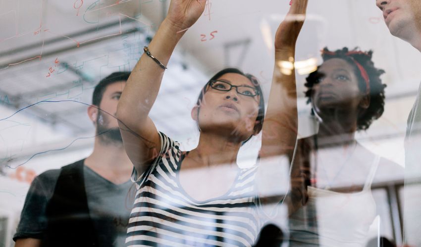 A diverse creative team brainstorming and writing ideas on a glass wall in an office