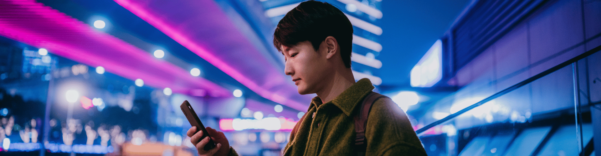 Man using a smartphone in a neon-lit city at night.