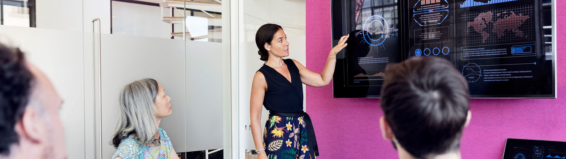 A woman giving a presentation in front of a large touchscreen