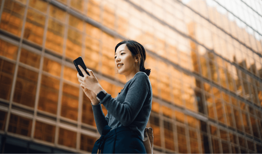 Person using smartphone outside modern glass building with golden reflections