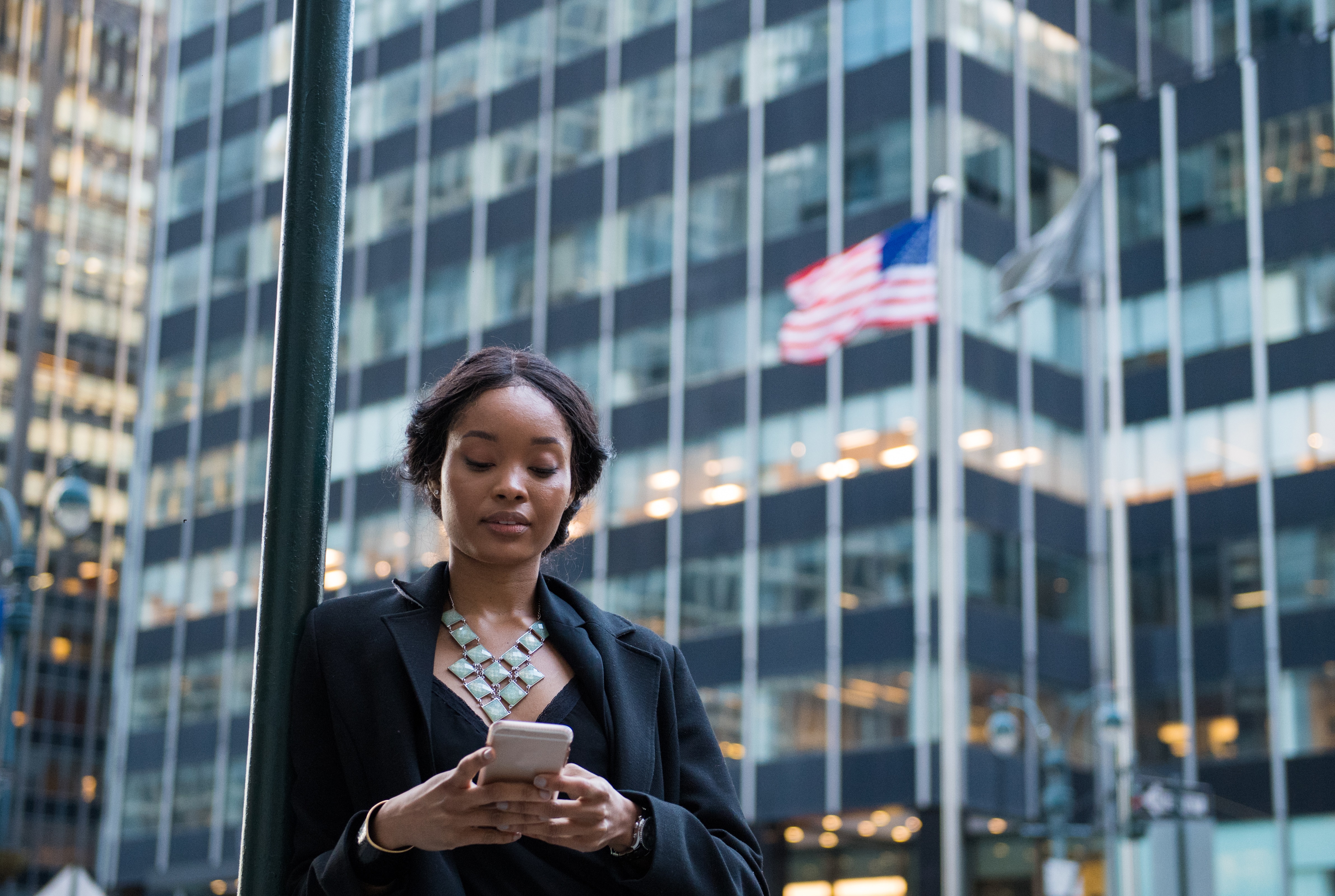 A professional woman using a smartphone in a city with an American flag background