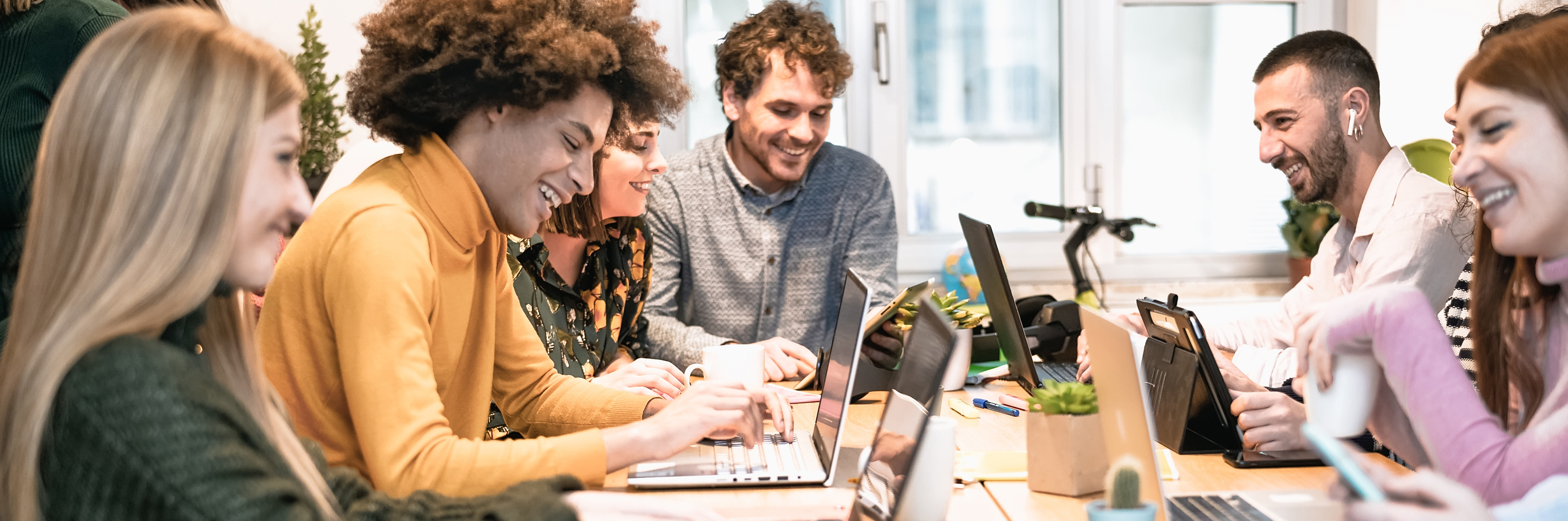 A group of laughing and smiling interns sitting around a table with their laptops