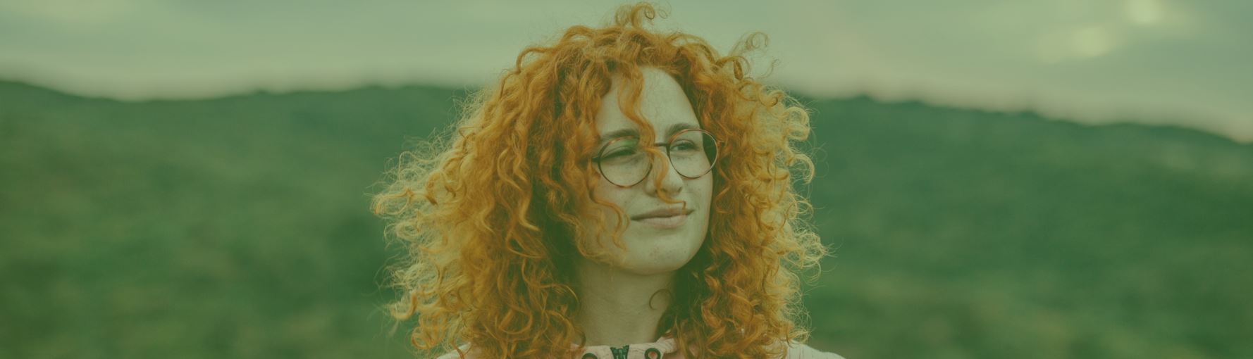 A woman wearing glasses with a hillside in the background