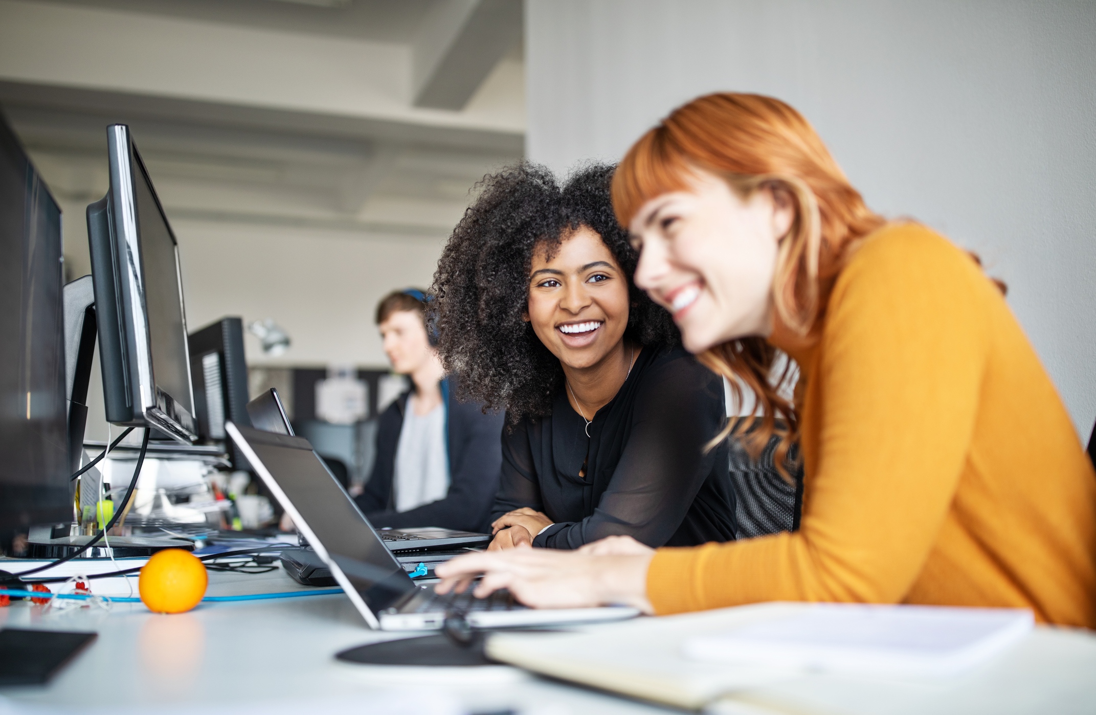 Two interns laughing together while working at their laptops