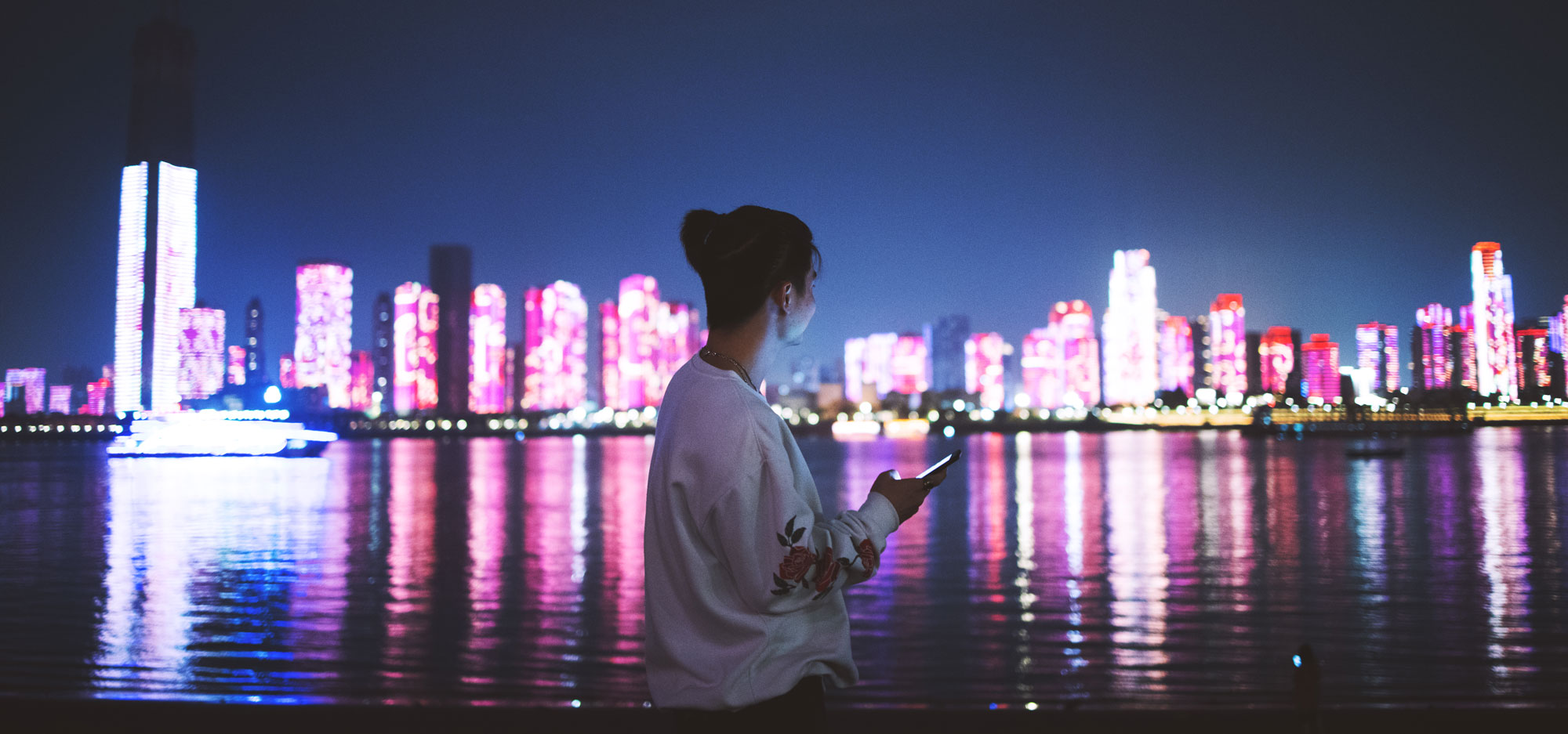 Woman using a mobile phone at night against a city skyline