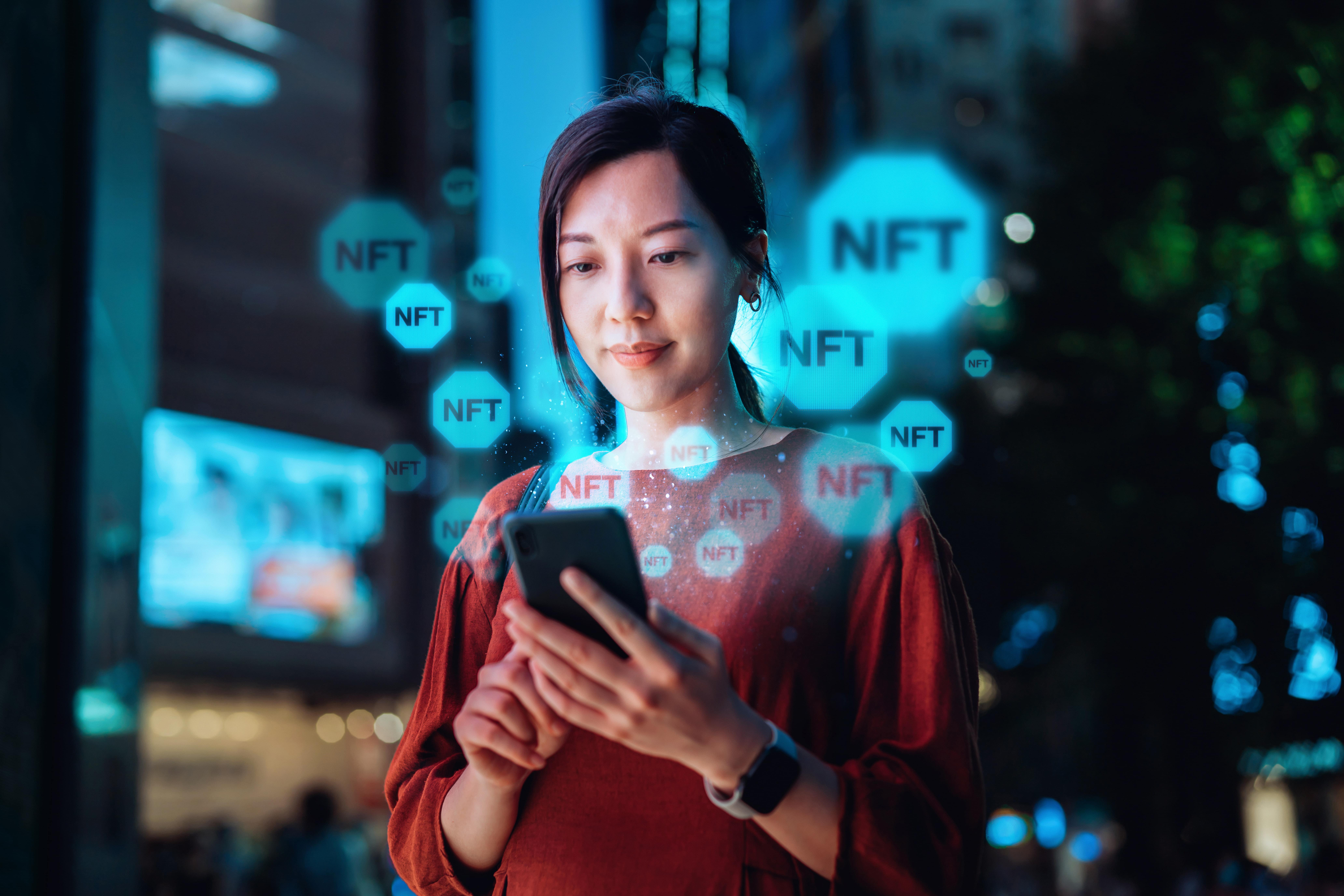 A woman looking at smart phone with an overlay of NFT logos