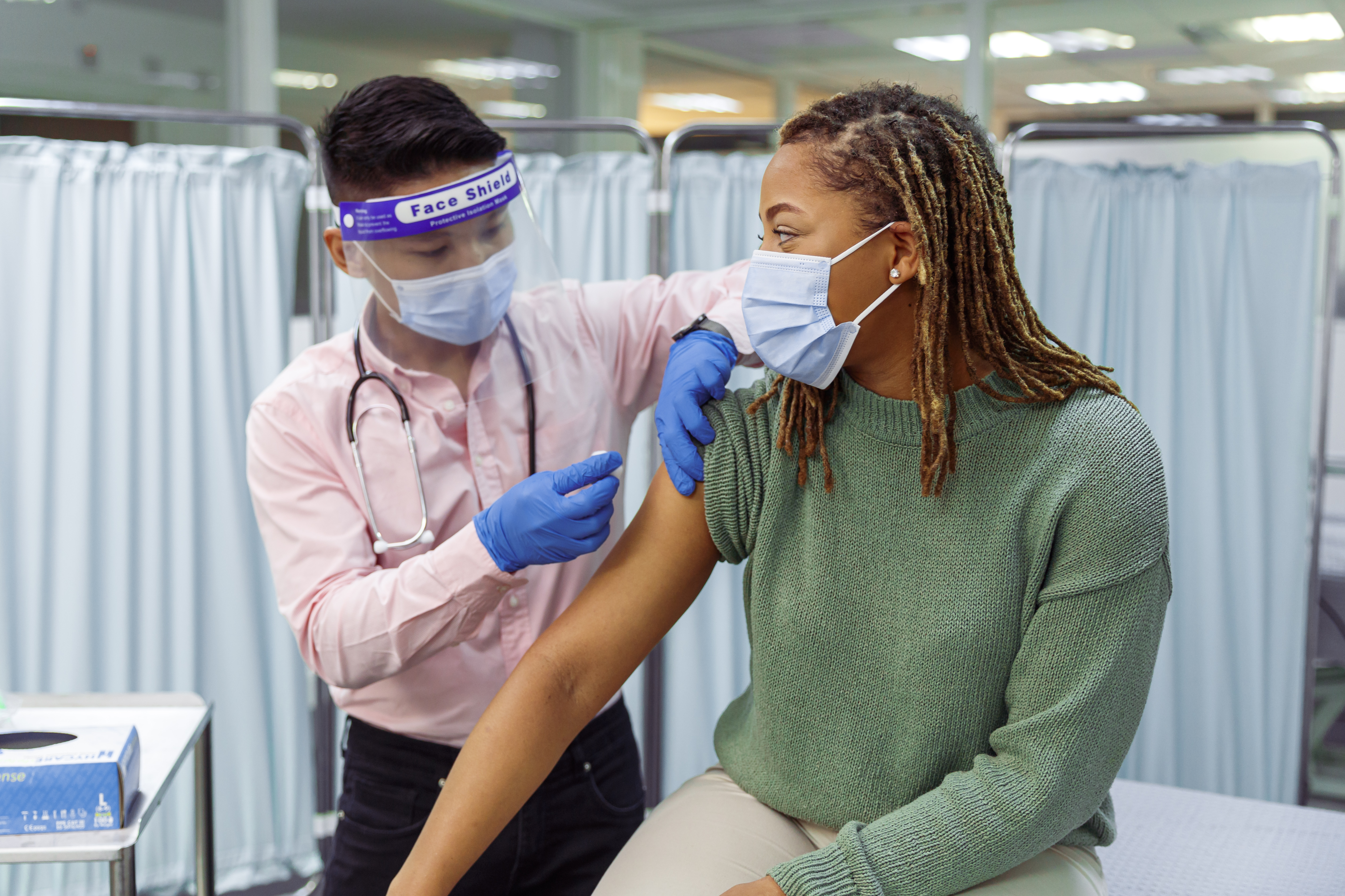 A woman wearing a facemask receiving a vaccine from someone in PPE