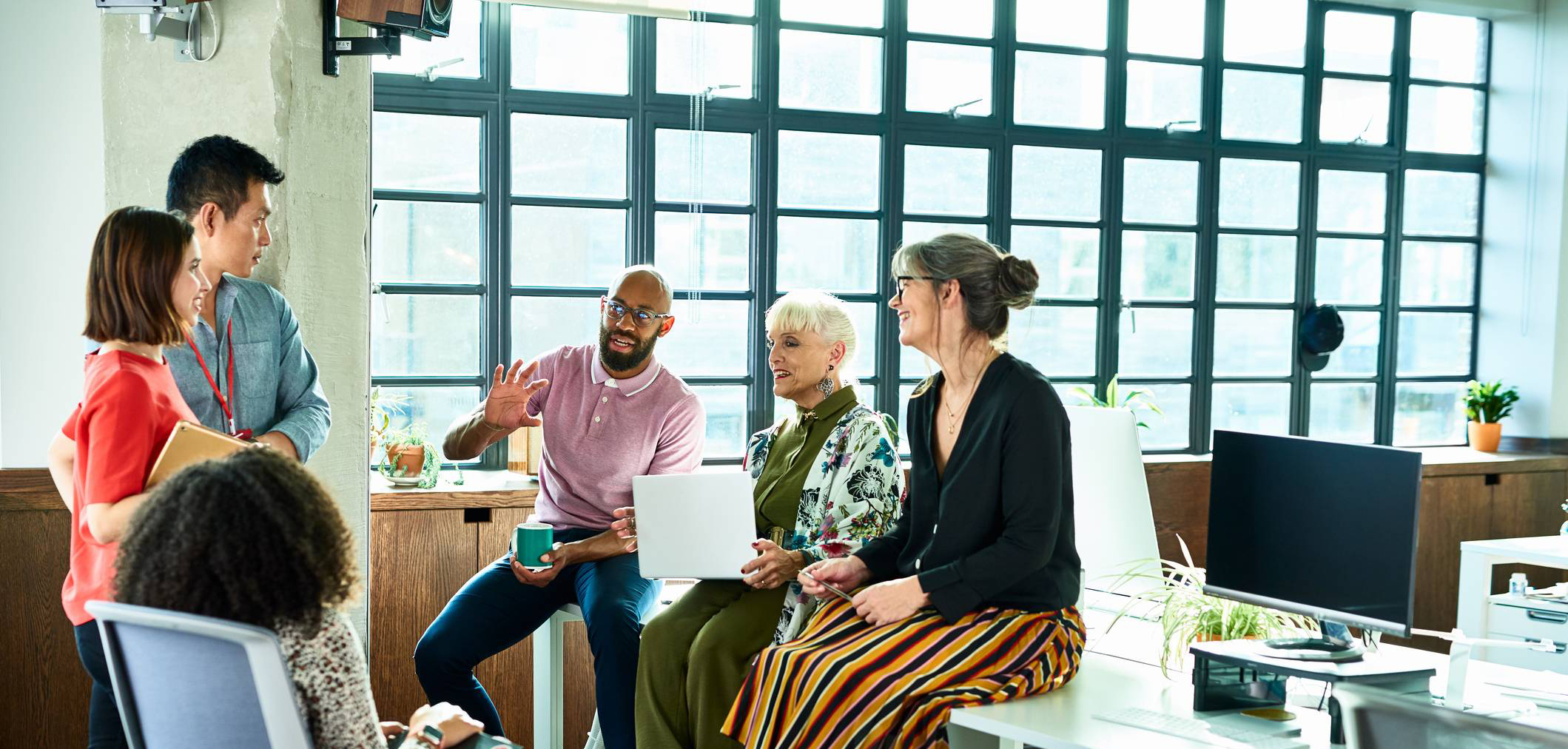Six people in relaxed conversation with a laptop and coffee