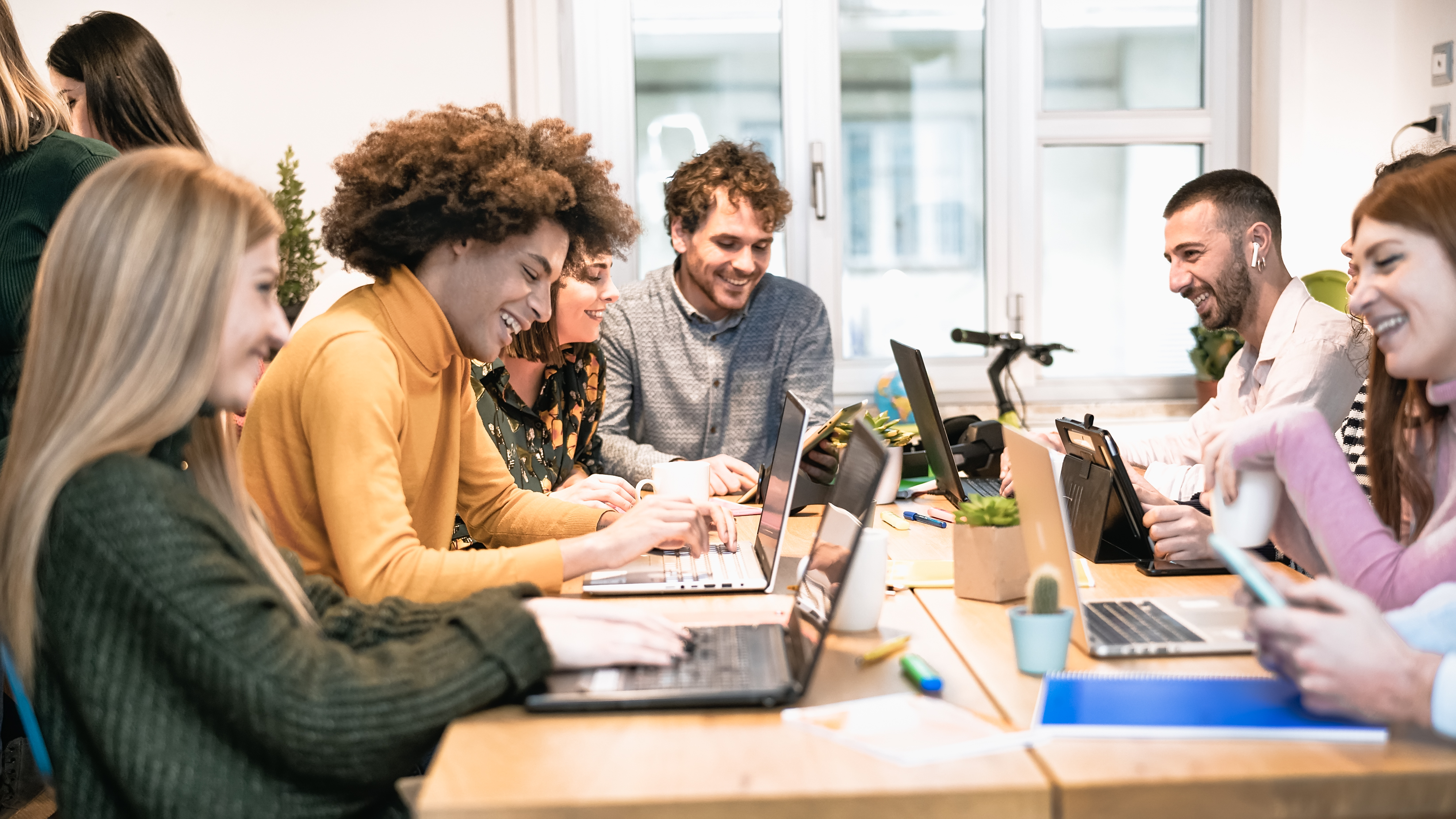 A group of laughing and smiling interns sitting around a table with their laptops