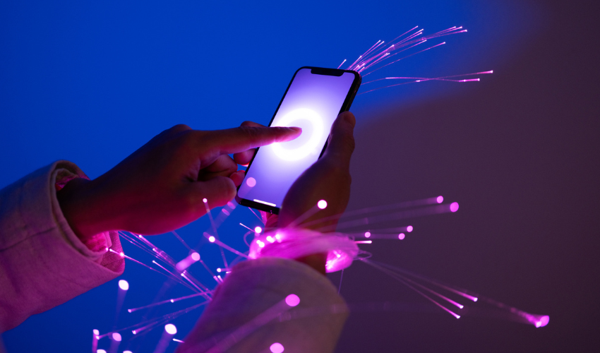 Person holding a smartphone surrounded by glowing pink fiber optic lights