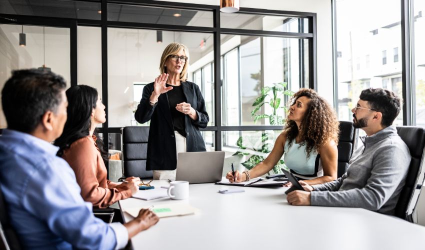A professional woman leads a meeting with diverse colleagues in a bright modern office