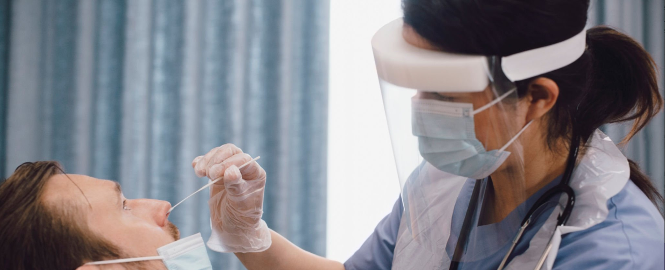 A woman wearing PPE taking nasal swab from a patient