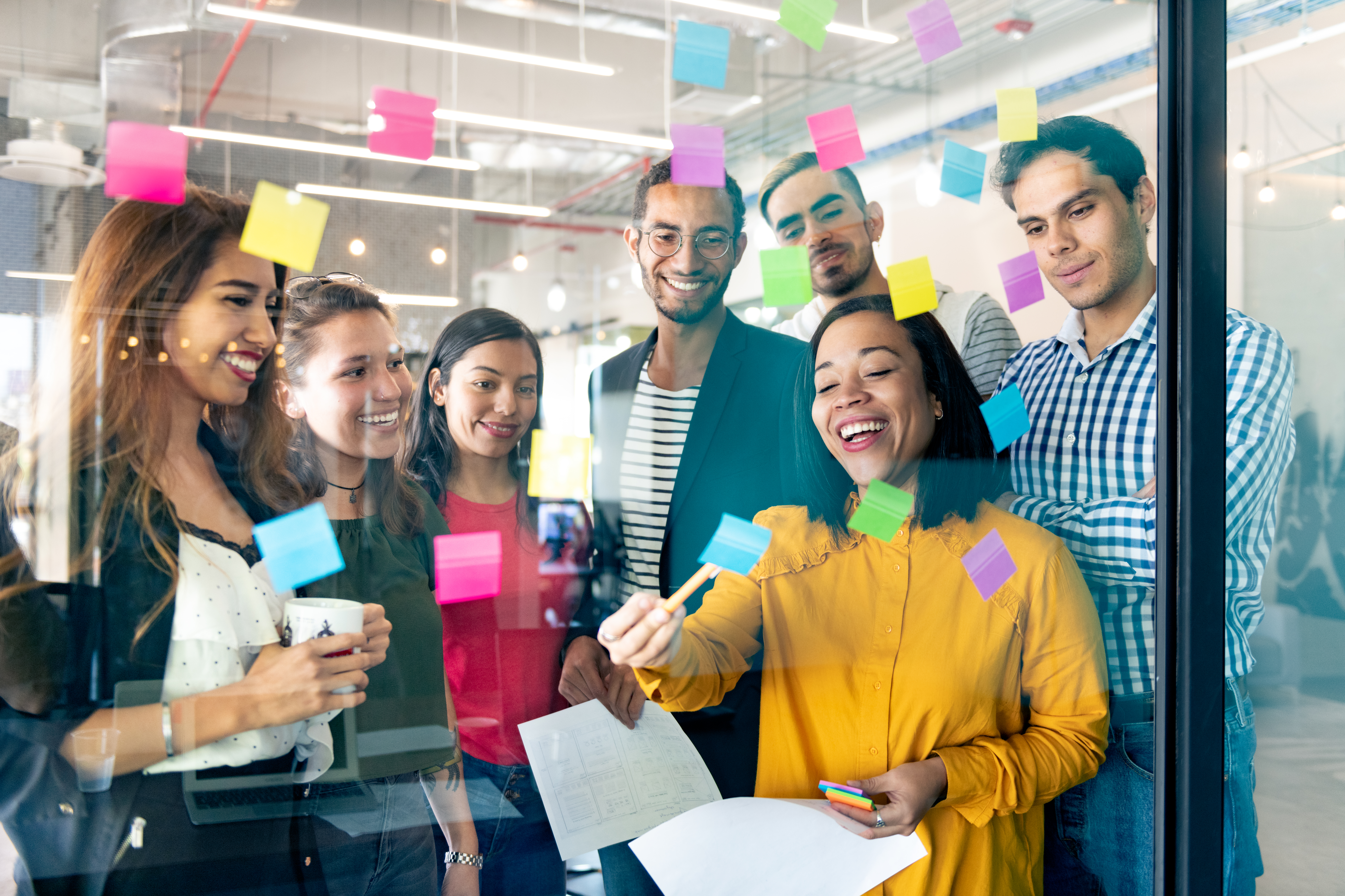 Group of coworkers looking at post-it notes on a glass wall