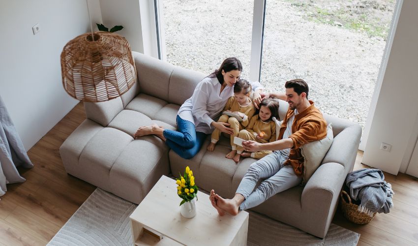 A family of four relaxes on a neutral sectional sofa while the father takes a selfie