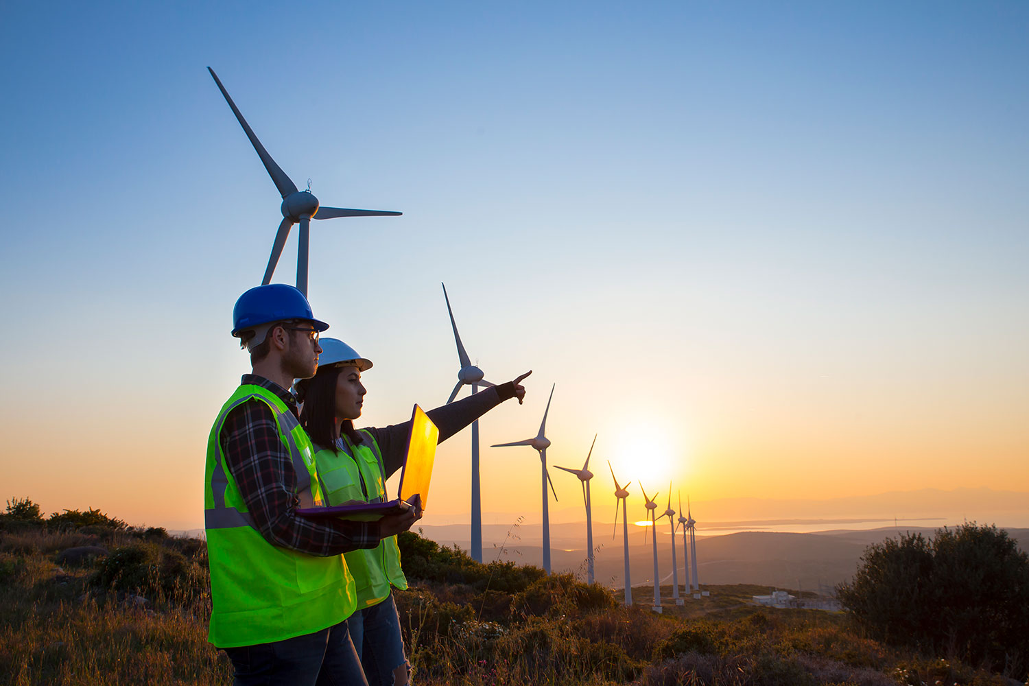 Two engineers with a laptop standing in front of some wind turbines