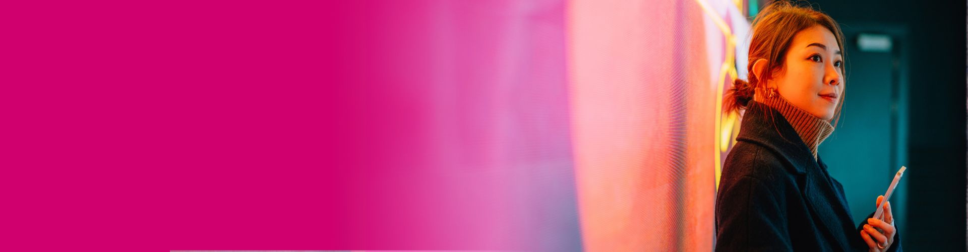 Woman against a pink wall holding a smartphone
