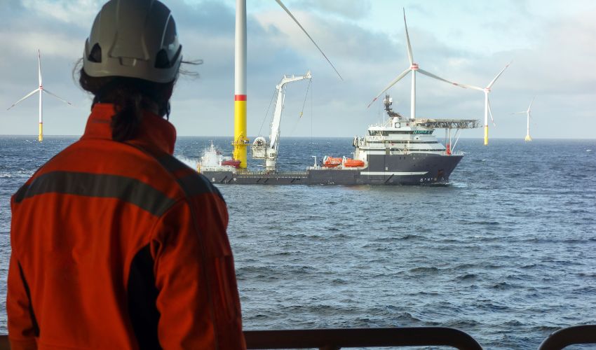 Engineer in high-visibility gear looks out at an offshore wind farm and service vessel
