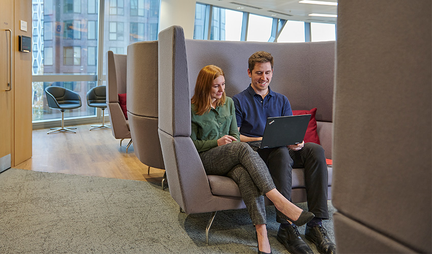 Two colleagues looking at laptop while sitting on a sofa in a relaxed and comfortable office environment