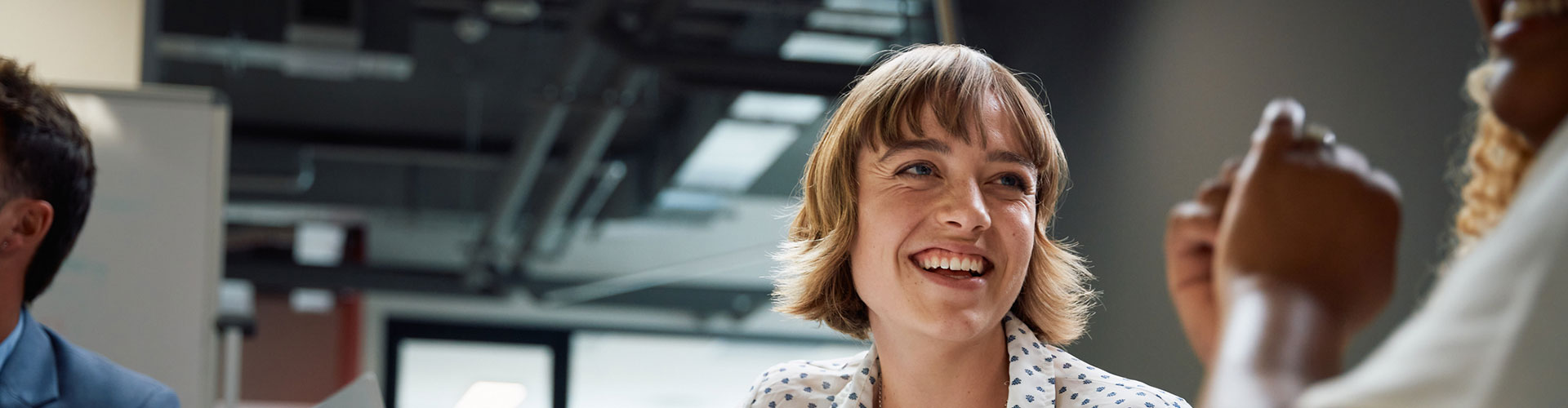 Three happy multiracial business people wearing businesswear smiling during discussion at meeting in office