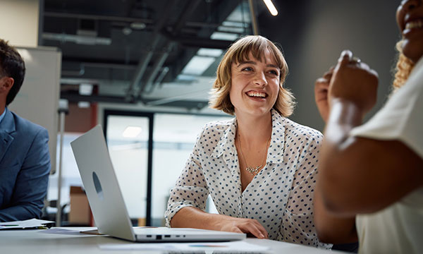 Three happy multiracial business people wearing businesswear smiling during discussion at meeting in office