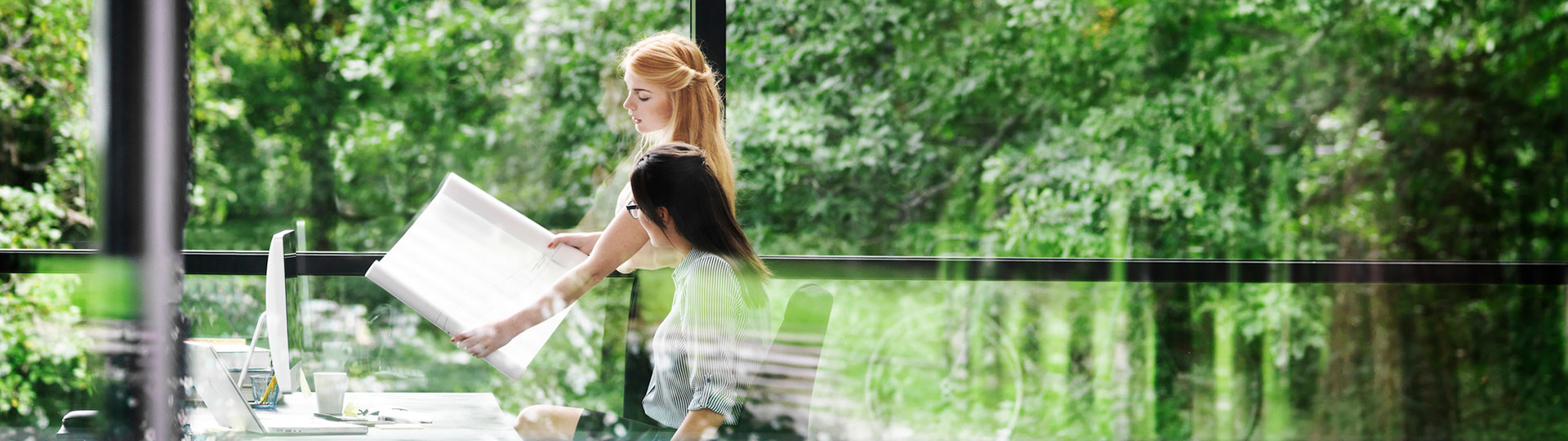 A pair of women discussing a hand-held plan with lush green vegetation in the background