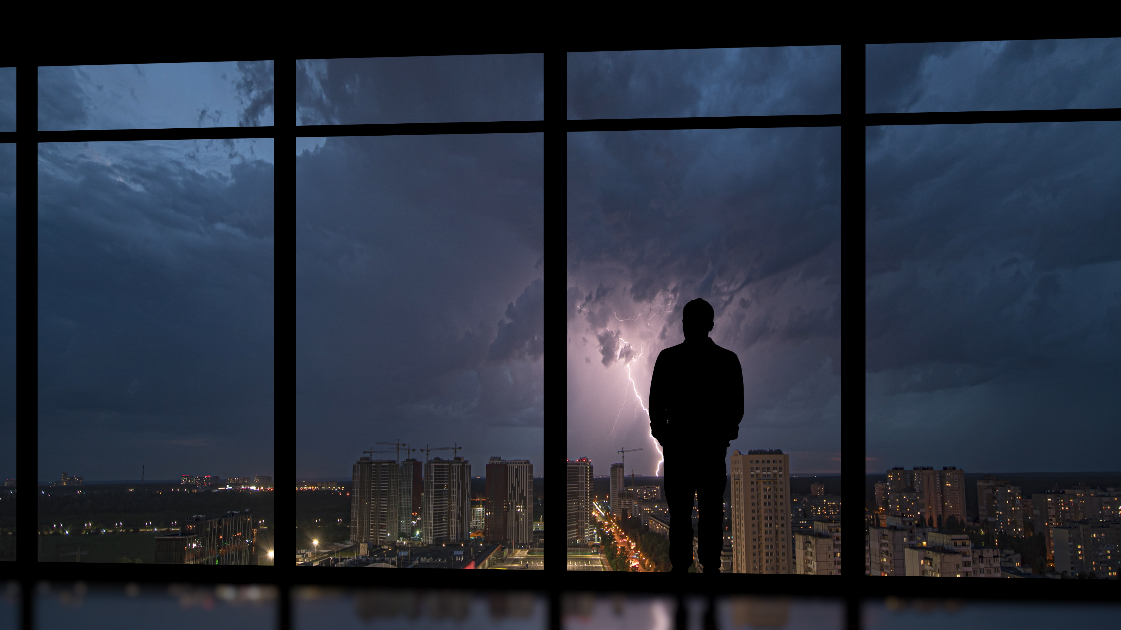 Man in office building looking out at lightning storm