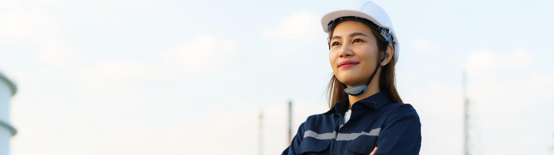 A woman in a hard hat with an industrial landscape in the background