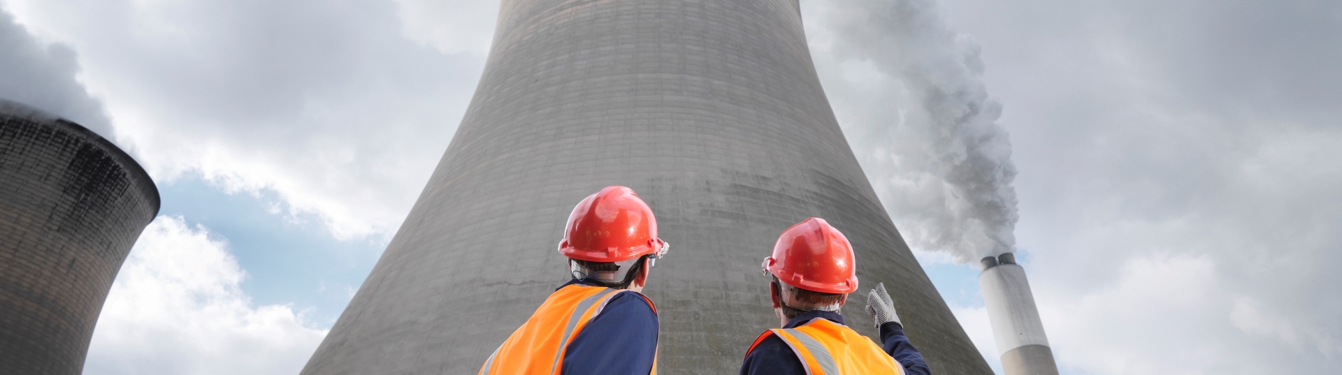 Two men in hard hats staring upwards at a cooling tower