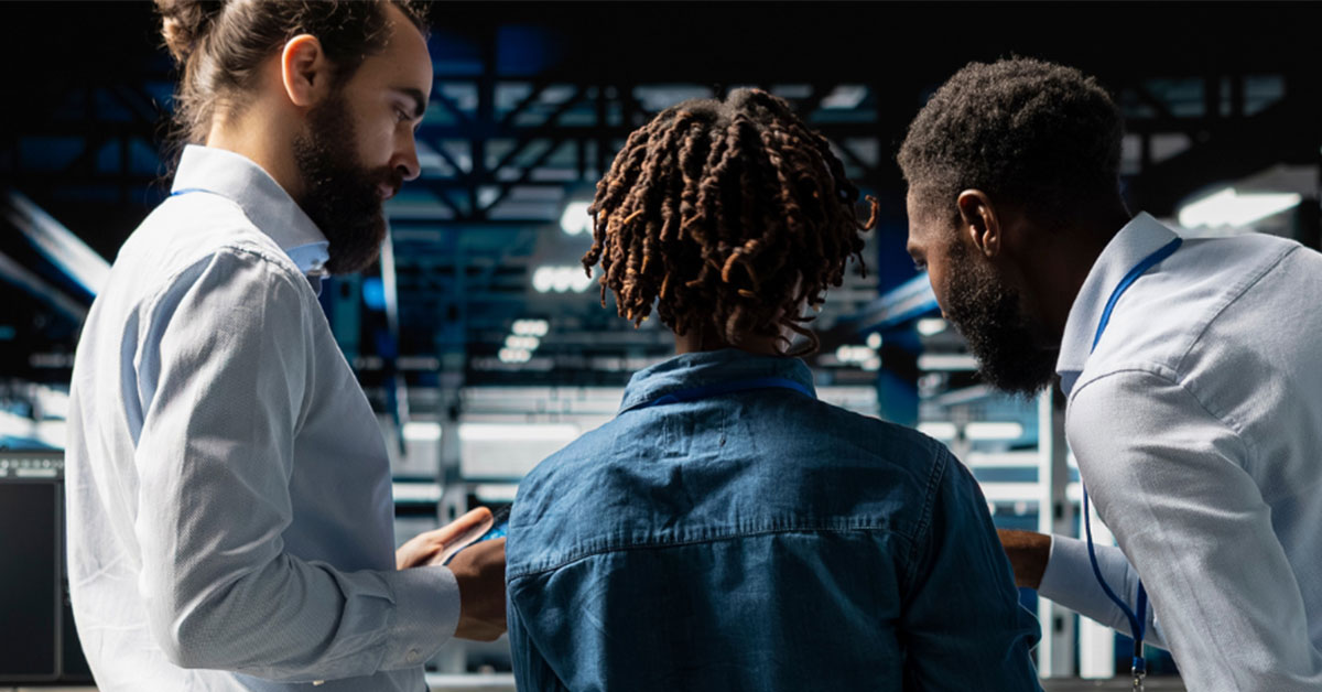 Three professionals collaborating and looking at a digital device in a modern data center