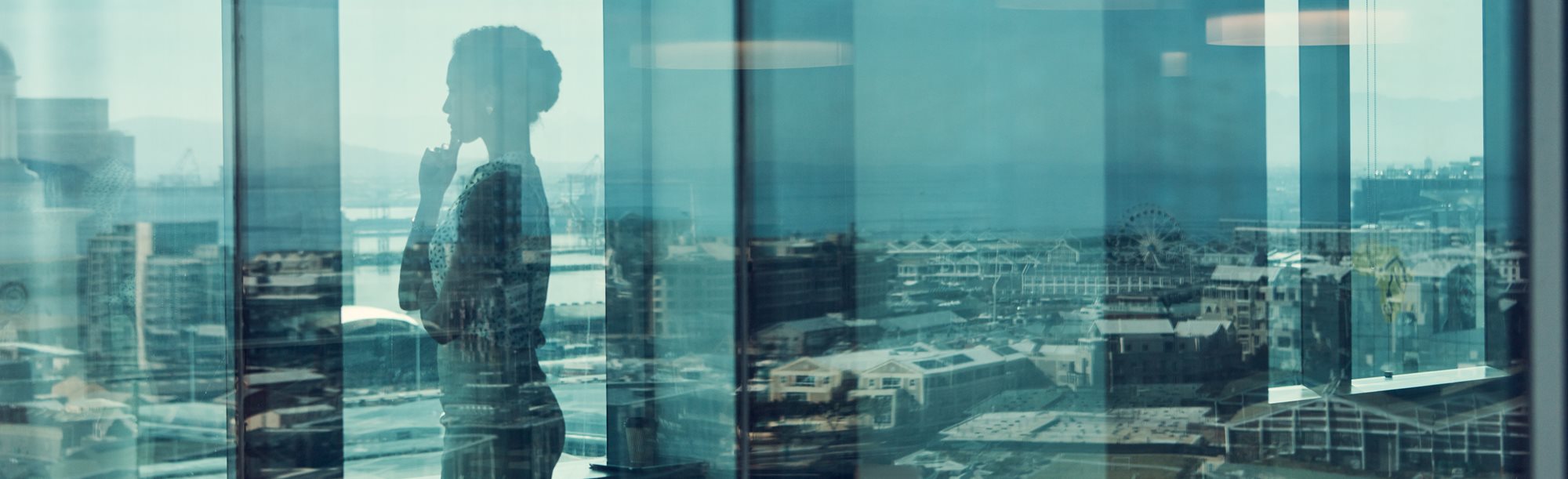 A thoughtful woman looking out of an office window over the city skyline