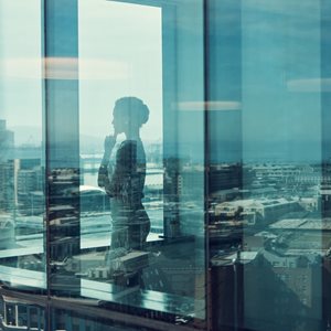 A thoughtful woman looking out of an office window over the city skyline