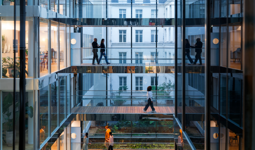 Modern glass office interior with people walking across skybridges over a garden courtyard