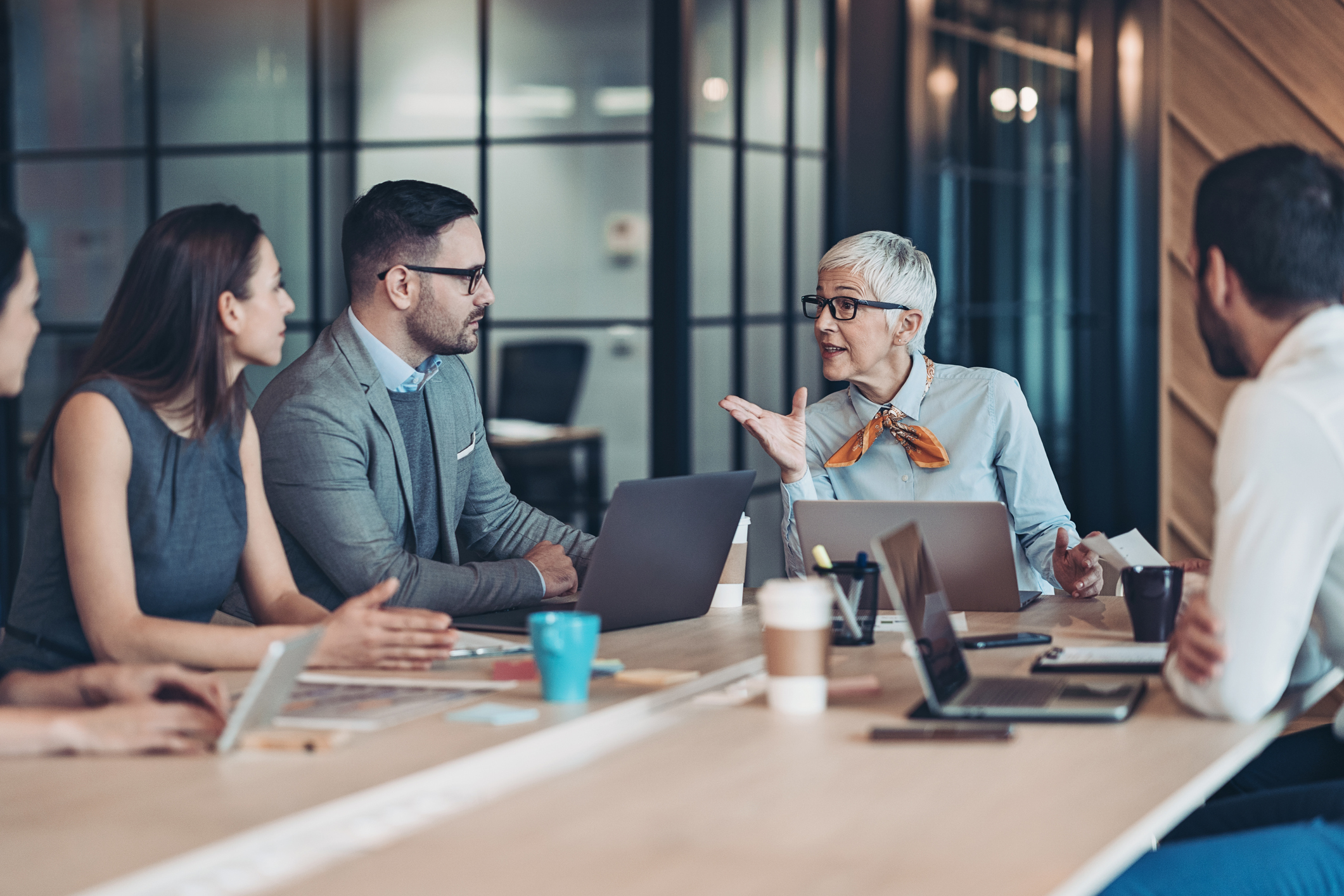 A diverse team of professionals discusses work around a table in a modern office