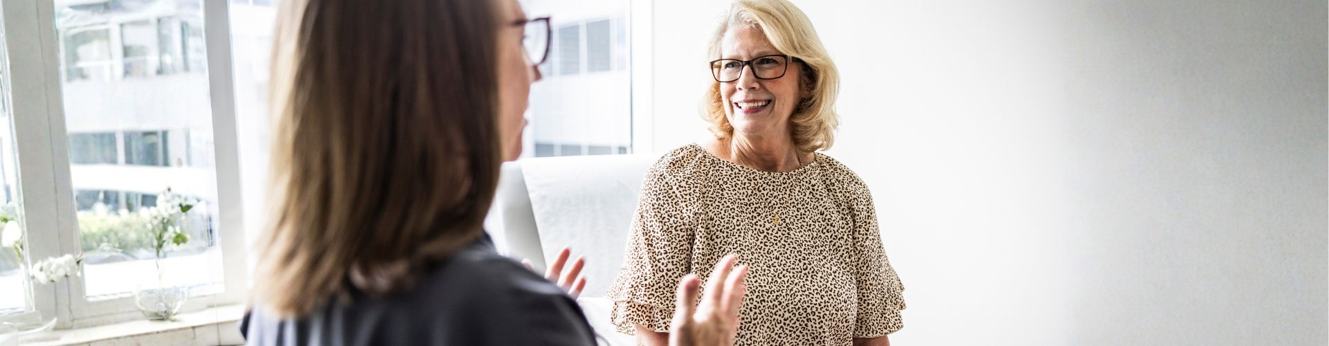 Two women in glasses having a positive, smiling conversation in a bright office