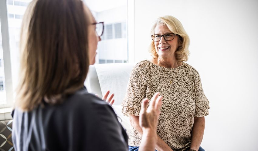 Two women in glasses having a positive, smiling conversation in a bright office