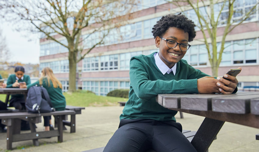 Child at school smiling while holding a smartphone
