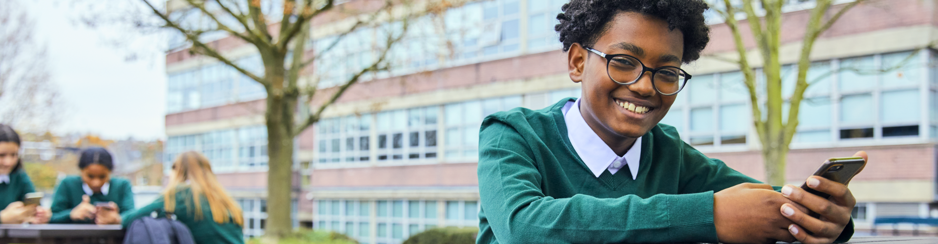Child at school smiling while holding a smartphone
