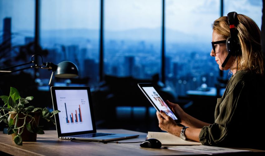 Woman in an office looking at reports on her laptop and tablet