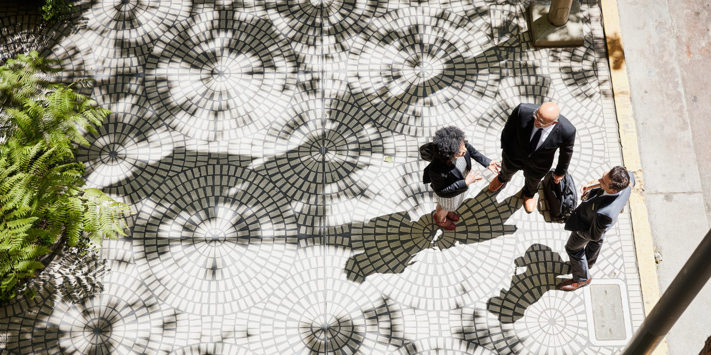Three business people having a conversation on tree lined sidewalk