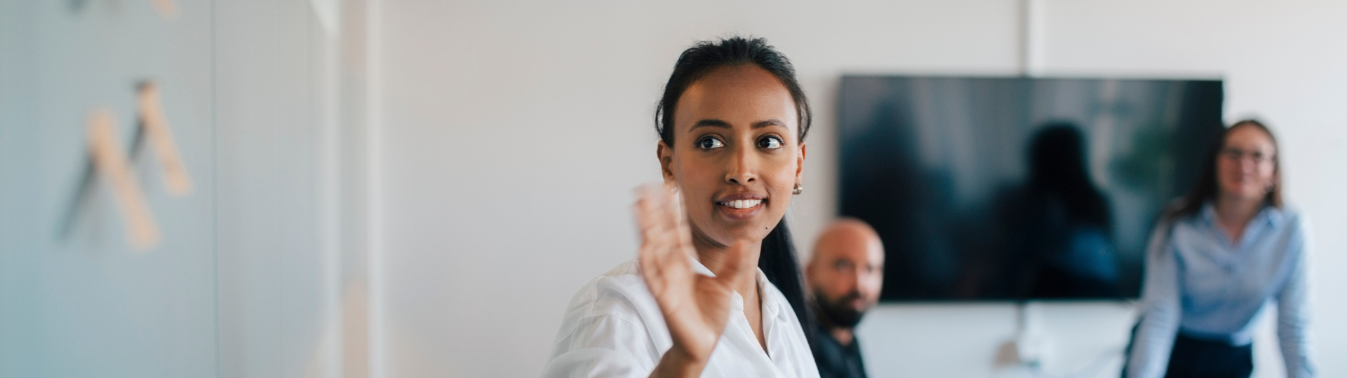 A woman waving while colleagues look on in the background of an office setting