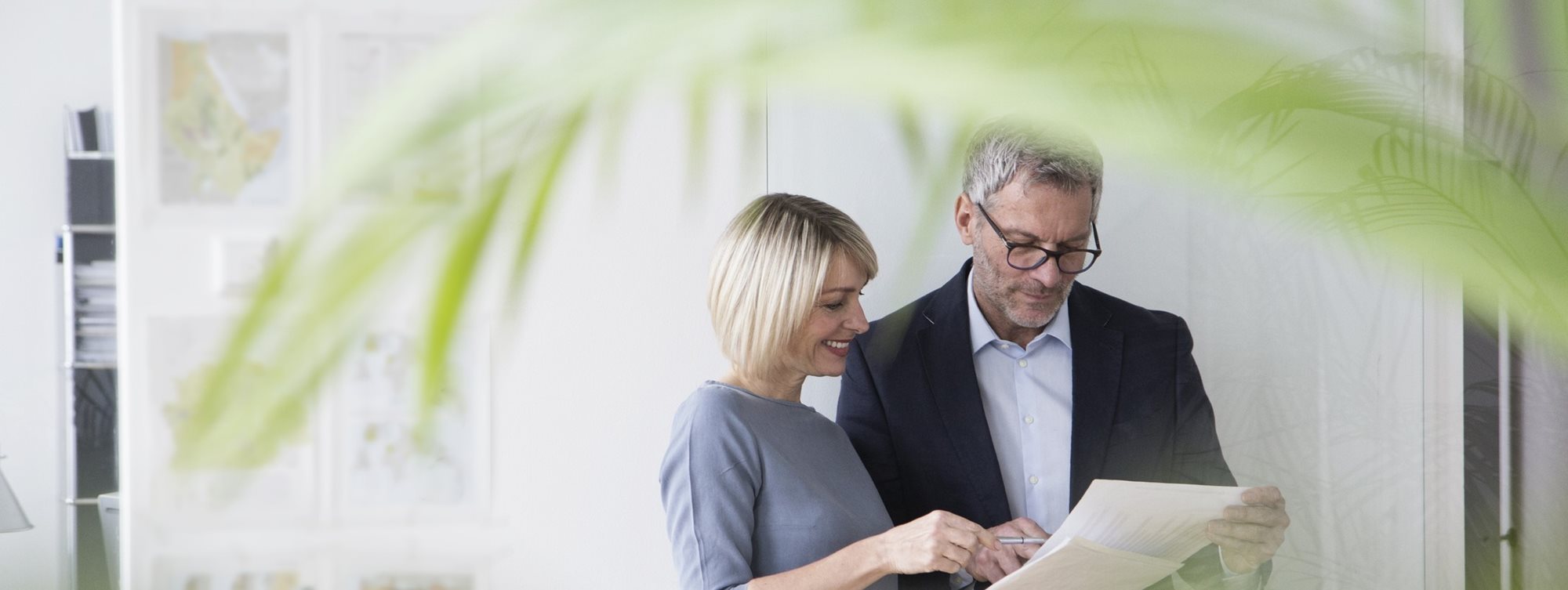 Two people looking at some paper with a palm frond in the foreground