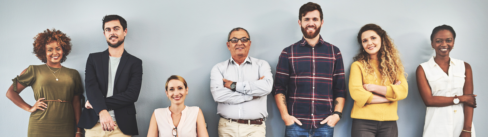 Seven smiling people in front of a grey wall