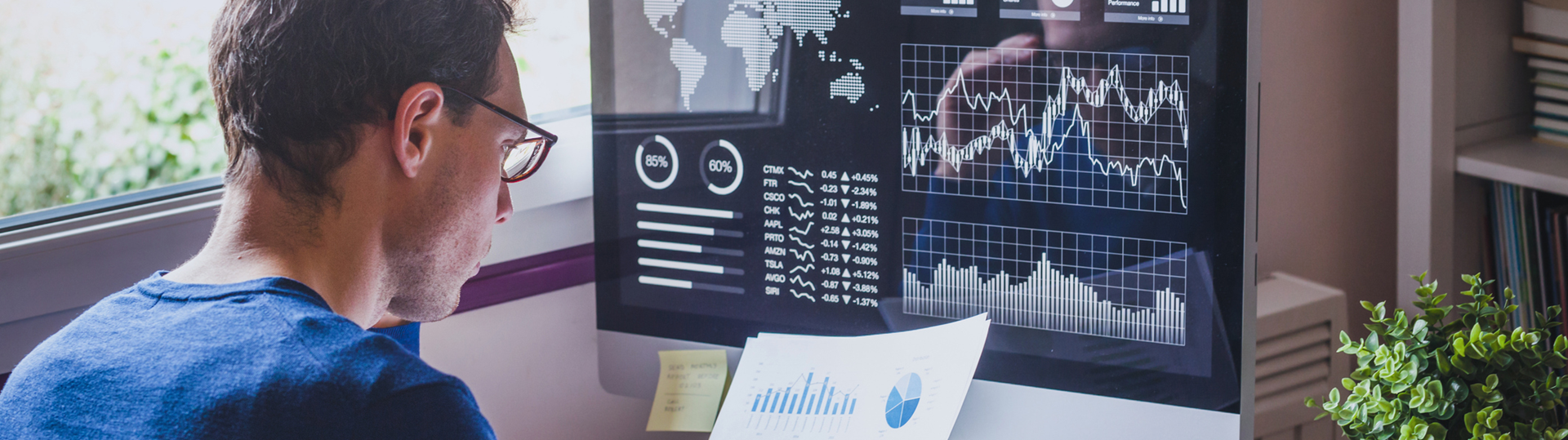 A man reading paper data reports and stocks graphs on his computer