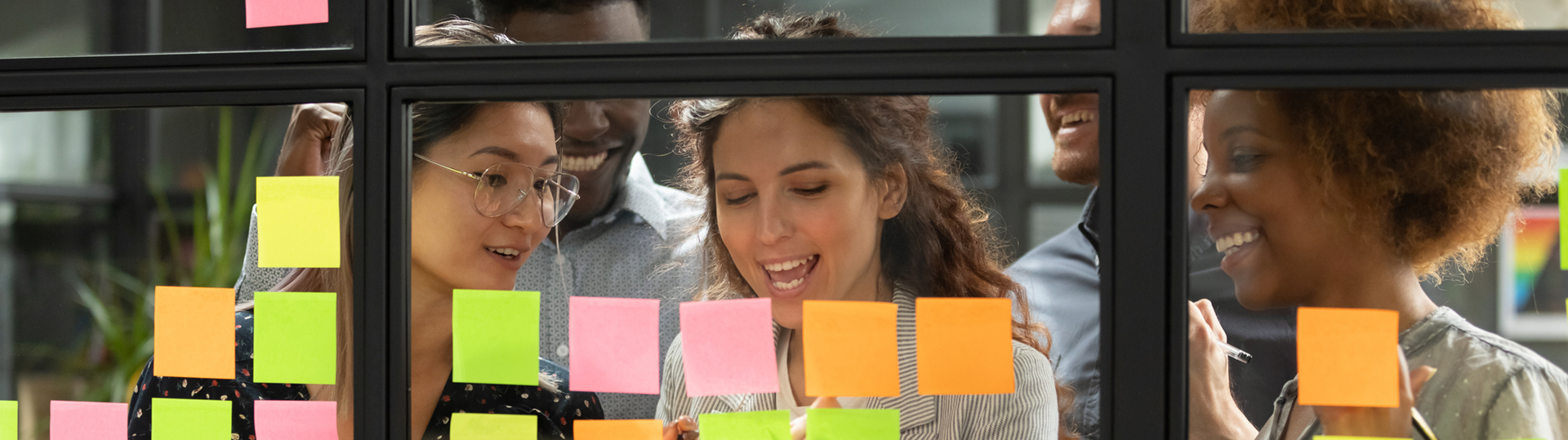Four people looking at post its on a glass interior window