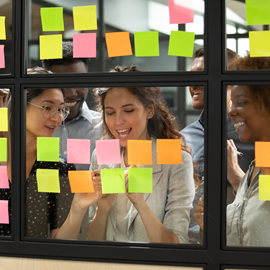 Four people looking at post its on a glass interior window
