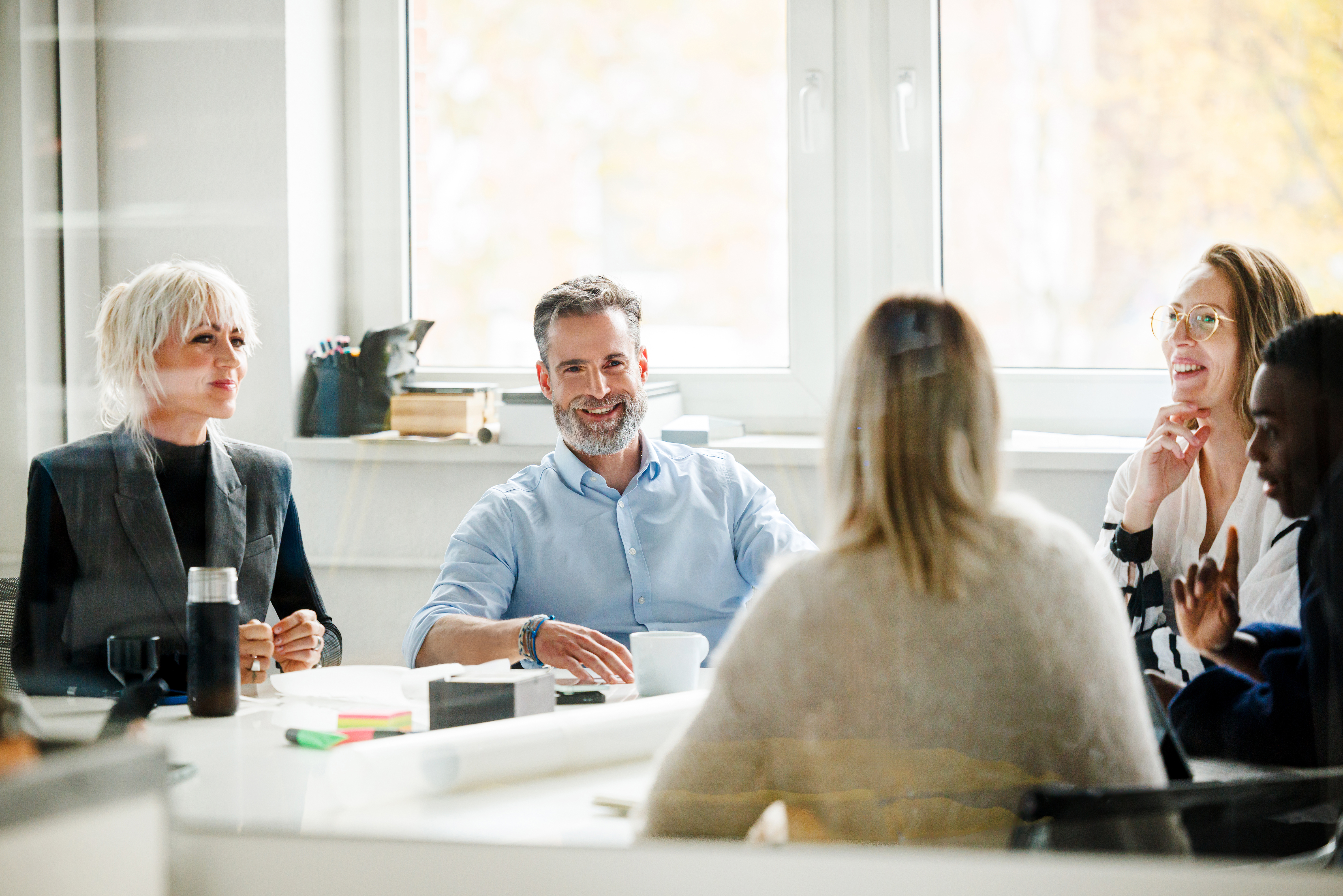 A group of diverse colleagues smiling and talking during a meeting in a bright office