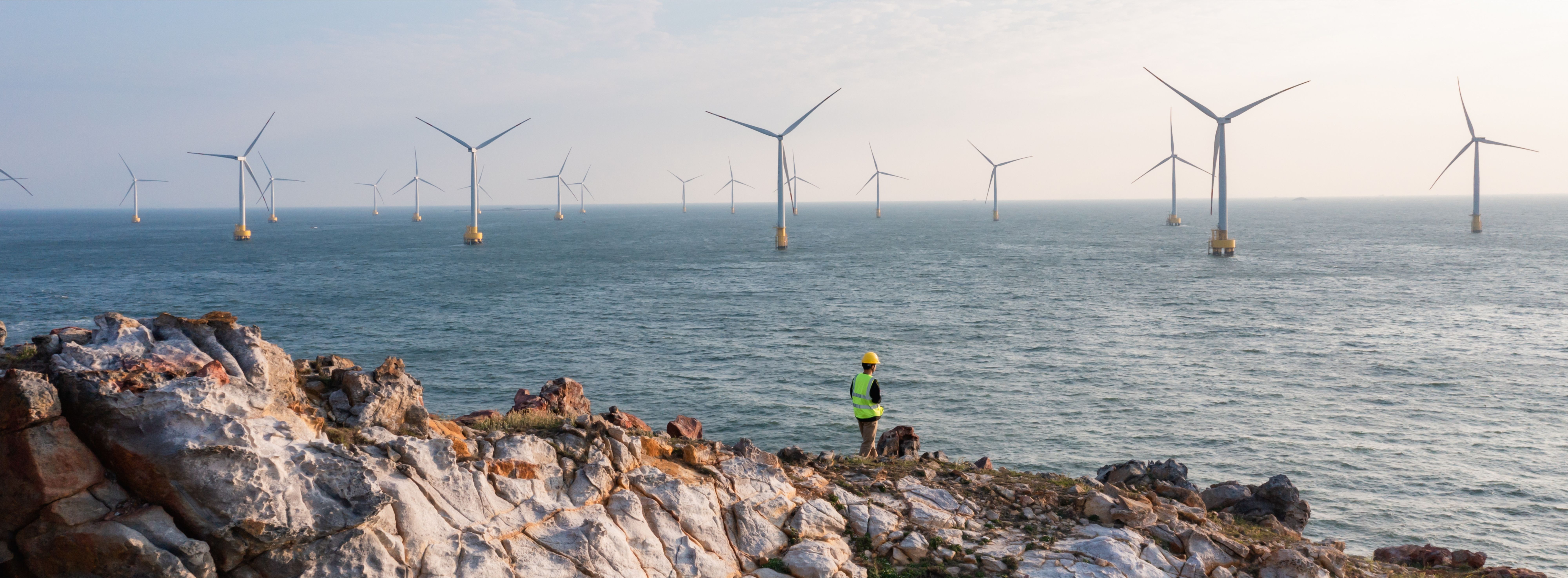 Worker looking across the sea to an offshore wind farm