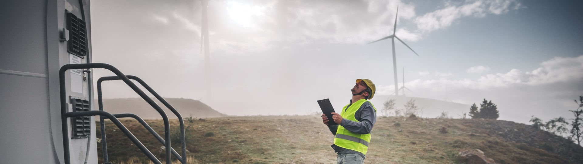 A man with a clipboard looking upwards at a wind turbine